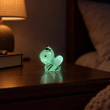 Miniature Glow Bee Assorted (1pc) glowing on a wooden table beside a warm lamp in a dimly lit room
