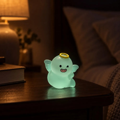 Miniature Glow Ghost Angel Doll Assorted (1pc) glowing on a wooden table beside a warm lamp in a dimly lit room