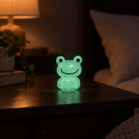 Miniature Glow Frog Assorted (1pc) glowing on a wooden table in a dimly lit room