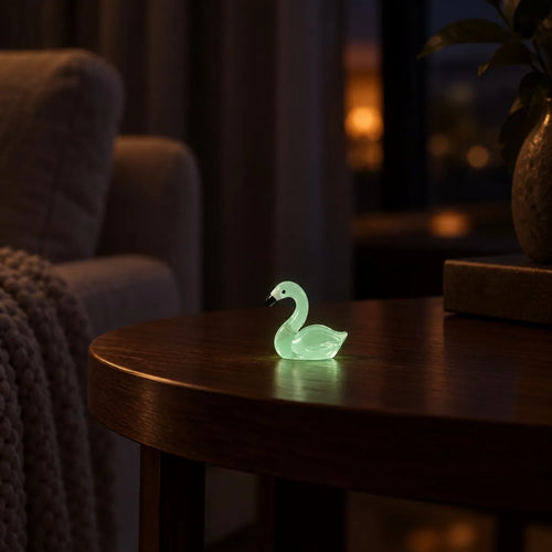 Miniature Glow Swan Assorted (1pc) glowing on a wooden table in a dimly lit room